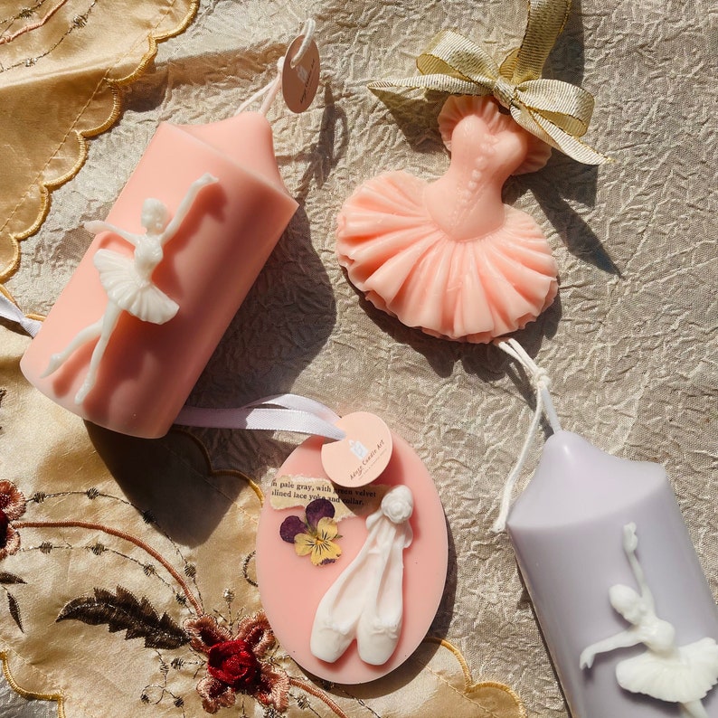 May include: Four pink and purple scented candles shaped like a ballerina, a tutu, a pair of ballet shoes, and a ballerina with a flower. The candles are decorated with white ballerina figures and flowers.