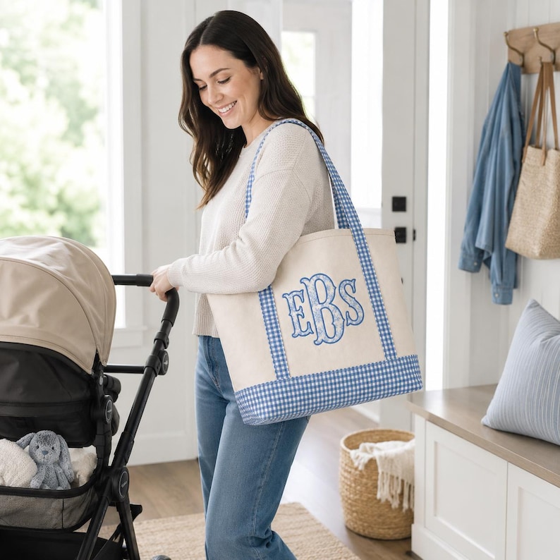 May include: A large off-white canvas tote bag featuring a blue and white gingham check pattern on the base and straps. The center of the bag displays a large, decorative embroidered monogram with the letters EBS in a blue floral print.
