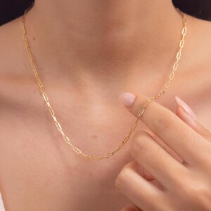 May include: A gold chain necklace with a delicate, linked design. The chain is made of small, rectangular links that are connected together to create a continuous loop.