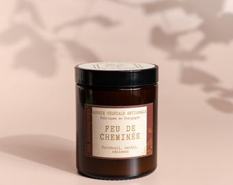 May include: A brown glass jar candle with a black lid. The label reads "FEU DE CHEMINÉE" with scent notes. The candle is labeled "Bougie Végétale Artisanale" and "Fabriquée en Bourgogne."