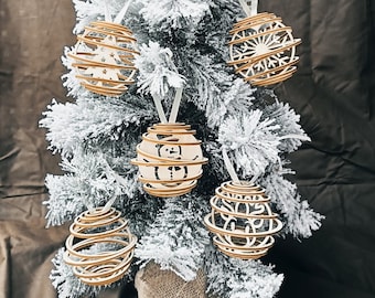Op de afbeelding: Een witte kunstkerstboom versierd met zes houten ornamenten. De ornamenten zijn bolvormig en hebben een geometrisch ontwerp. De boom is bedekt met witte kunstneeuw.
