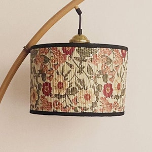 Puede incluir: Una lámpara de pie de bambú con una pantalla de lámpara con estampado floral. La pantalla tiene un ribete negro y un fondo blanco con flores rojas, rosas y verdes.