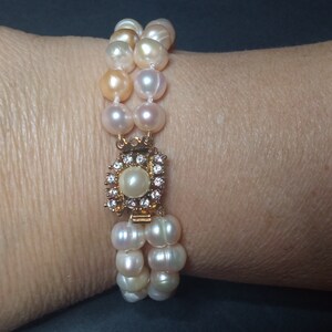 Può includere: Un braccialetto di perle a doppio filo con una chiusura dorata incastonata con piccoli diamanti. Le perle sono un mix di colori bianco e crema.