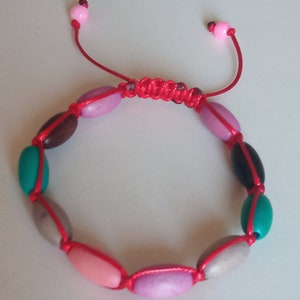 May include: A red string bracelet with colourful oval beads. The beads are pink, brown, grey, teal, and black.