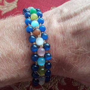 May include: A multi-coloured beaded bracelet with blue, green, brown, white and pink beads. The bracelet is made with a knotted cord.