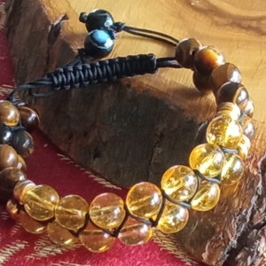 May include: A brown and gold beaded bracelet with a black cord. The bracelet has two rows of beads, one row of brown tiger's eye beads and one row of gold beads.