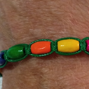 May include: A green string bracelet with colorful wooden beads. The beads are orange, yellow, pink, and green.