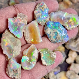 Könnte beinhalten: Eine Sammlung von rohen Opal-Steinen in verschiedenen Schattierungen von Weiß, Grün und Orange. Die Steine sind irisierend und haben ein natürliches, rohes Aussehen.