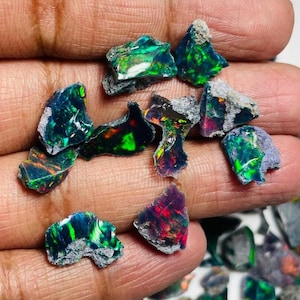 以下が含まれることがあります： 原石のブラックオパール宝石のコレクション。オパールは、暗くほぼ黒色のベースに対して、緑、青、赤、黄色の鮮やかな閃光を示しています。石は自然で未研磨の外観をしています。