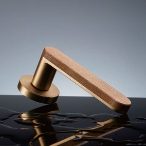 May include: A gold door handle with a wooden accent. The handle is on a black surface with water droplets.