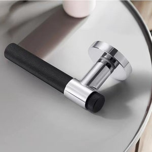 May include: A black and chrome door handle with a textured grip. The handle is shown on a gray surface.