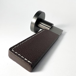 May include: A modern door handle with a brown leather wrap and white stitching. The handle is made of metal and has a brushed nickel finish.