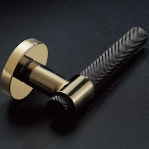May include: A gold door handle with a black, textured grip. The handle has a round base and a cylindrical grip.