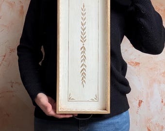 May include: A white wooden serving tray with a gold leaf design. The tray has two metal handles and a rectangular shape.