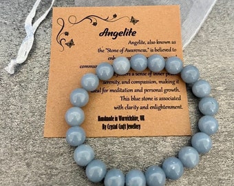 Puede incluir: Un brazalete de angélita azul claro con 14 cuentas. El brazalete está sobre una tarjeta marrón con el texto "Angélita, también conocida como la "Piedra de la Conciencia", se cree que mejora... una sensación de paz interior, serenidad y compasión, lo que la convierte en una herramienta ideal para la meditación y el crecimiento personal. Esta piedra azul se asocia con la claridad y la iluminación. Hecho a mano en Warwickshire, Reino Unido por Crystal Craft Jewellery."