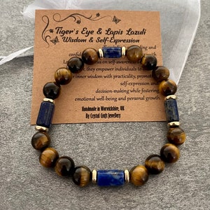 Puede incluir: Pulsera de cuentas con piedras de ojo de tigre y lapislázuli. La pulsera combina cuentas marrones y azul oscuro, con detalles dorados. Una etiqueta dice "Tiger's Eye & Lapis Lazuli Wisdom & Self-Expression" y "Handmade in Warwickshire, UK".