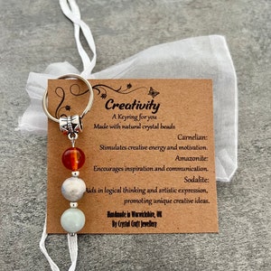 May include: A silver keyring with three beads: carnelian, amazonite, and sodalite. The keyring is labelled "Creativity" and includes the text "A Keyring for you Made with natural crystal beads".