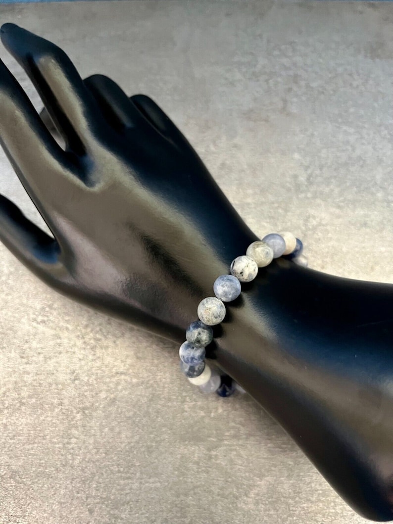 May include: A blue and white gemstone bracelet with round beads. The bracelet is made of natural stones and is approximately 7 inches in length.