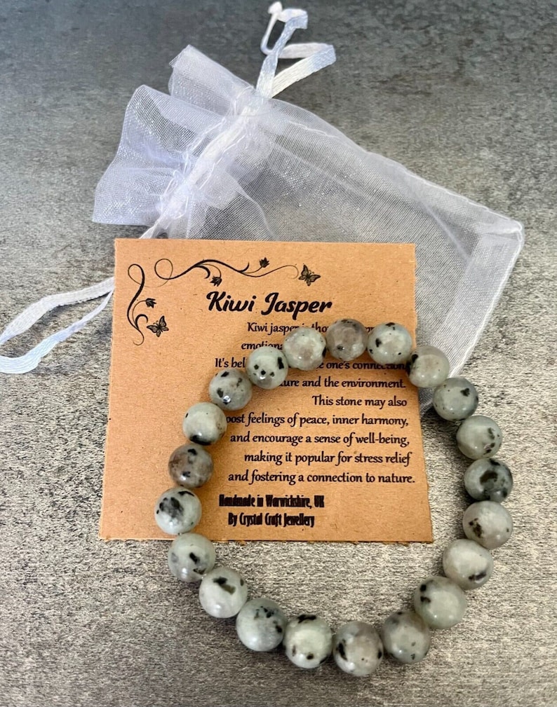 May include: A green and black kiwi jasper beaded bracelet with a brown card that reads "Kiwi Jasper" and includes information about the stone's properties. The bracelet is handmade in Warwickshire, UK by Crystal Craft Jewellery.