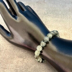 May include: A green and black gemstone bracelet with round beads. The bracelet is on a black mannequin wrist.