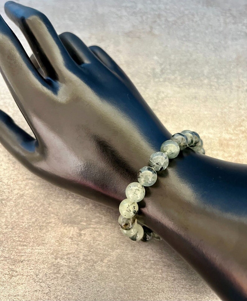 May include: A green and black gemstone bracelet with round beads. The bracelet is on a black mannequin wrist.