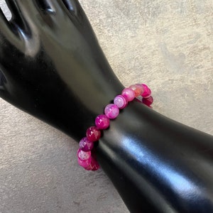 May include: A pink and white agate beaded bracelet. The beads are round and have a natural, polished finish.