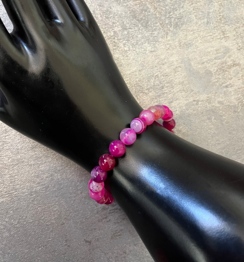 May include: A pink and white agate beaded bracelet. The beads are round and have a natural, polished finish.
