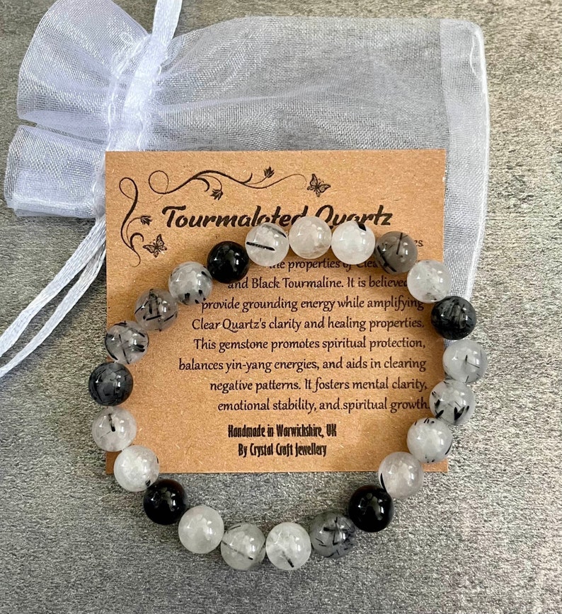 May include: Black and clear crystal beaded bracelet with a brown card that reads "Tourmalated Quartz" and describes the properties of the gemstones. The card also says "Handmade in Warwickshire, UK By Crystal Croft Jewellery".