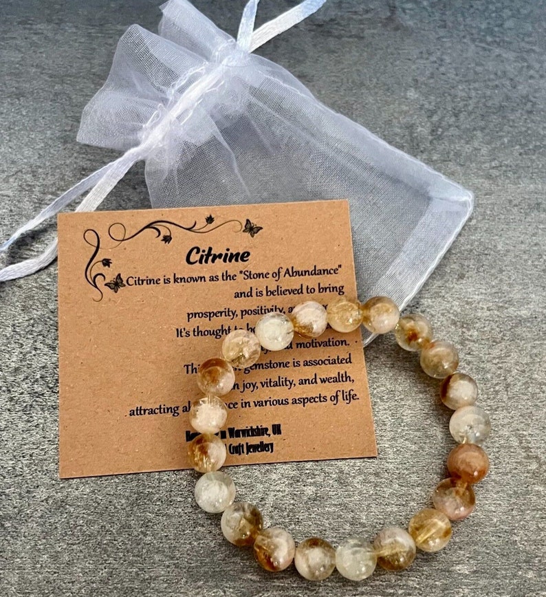 May include: Citrine gemstone bracelet with a brown card that reads "Citrine is known as the 'Stone of Abundance' and is believed to bring prosperity, positivity, and motivation. This gemstone is associated with joy, vitality, and wealth, attracting abundance in various aspects of life."