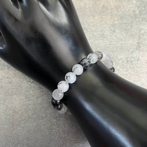 May include: A bracelet made of white and black gemstone beads. The beads are round and have a smooth, polished finish. The bracelet is strung on a clear elastic cord.