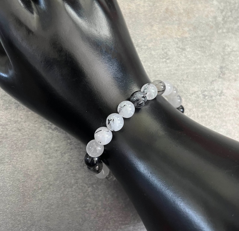 May include: A bracelet made of white and black gemstone beads. The beads are round and have a smooth, polished finish. The bracelet is strung on a clear elastic cord.