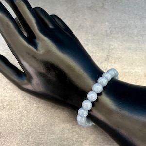 Puede incluir: Un brazalete de piedras preciosas azul claro con cuentas redondas. El brazalete est&aacute; en una mano de maniqu&iacute; negra.