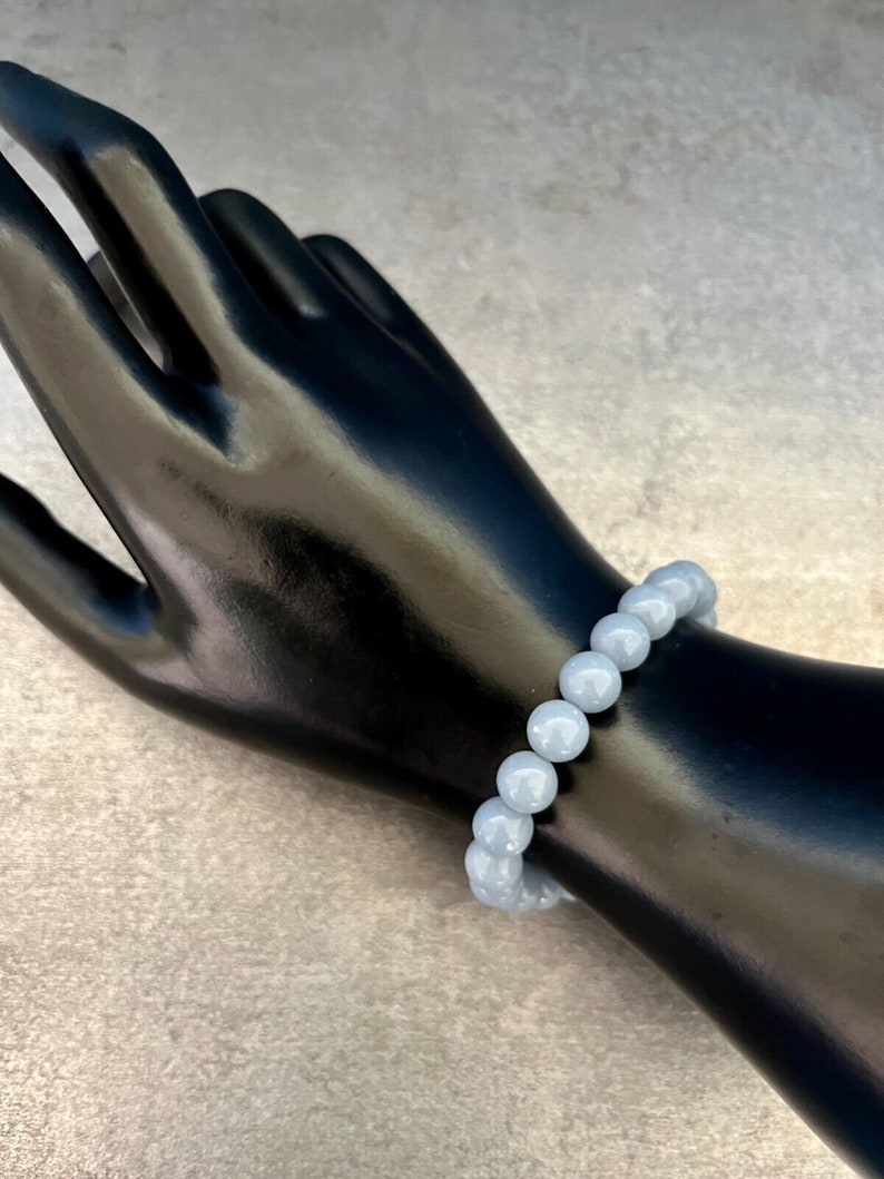 Puede incluir: Un brazalete de piedras preciosas azul claro con cuentas redondas. El brazalete est&aacute; en una mano de maniqu&iacute; negra.