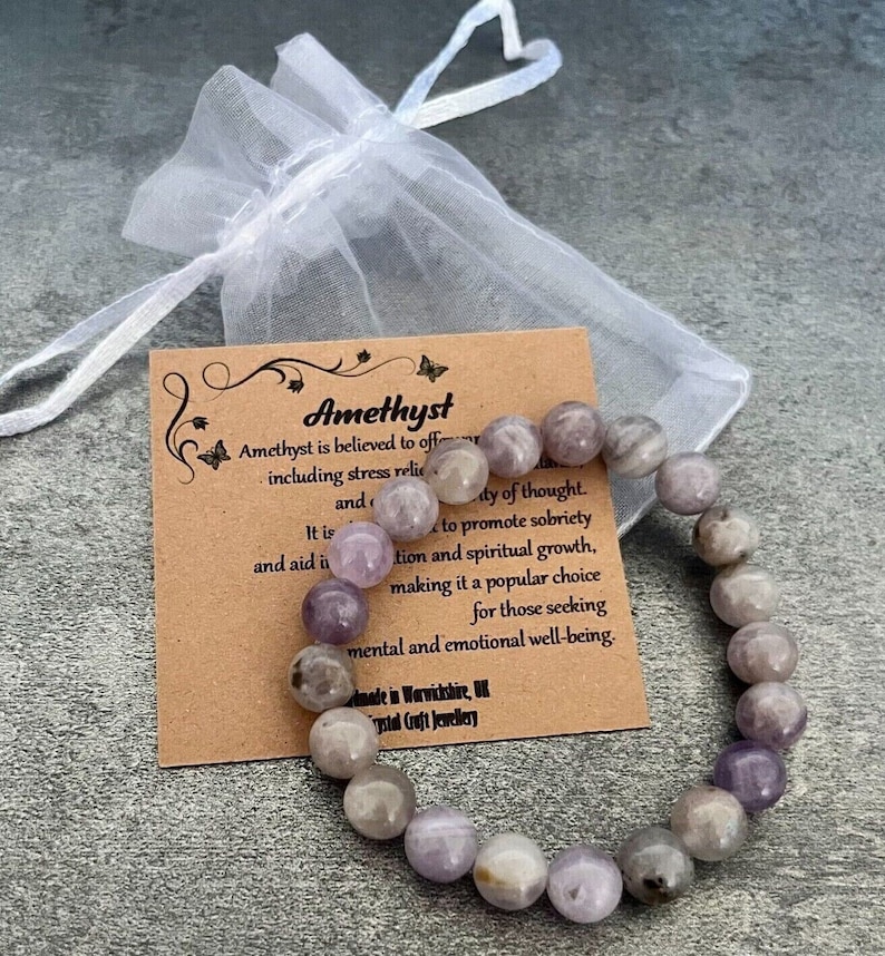 May include: Amethyst bracelet made of purple and white stones. The bracelet is on a brown card with the text "Amethyst" and information about the stone's properties.
