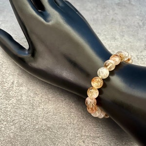 May include: A bracelet made of light pink, white, and gold-toned round beads. The beads have a translucent, cloudy appearance.