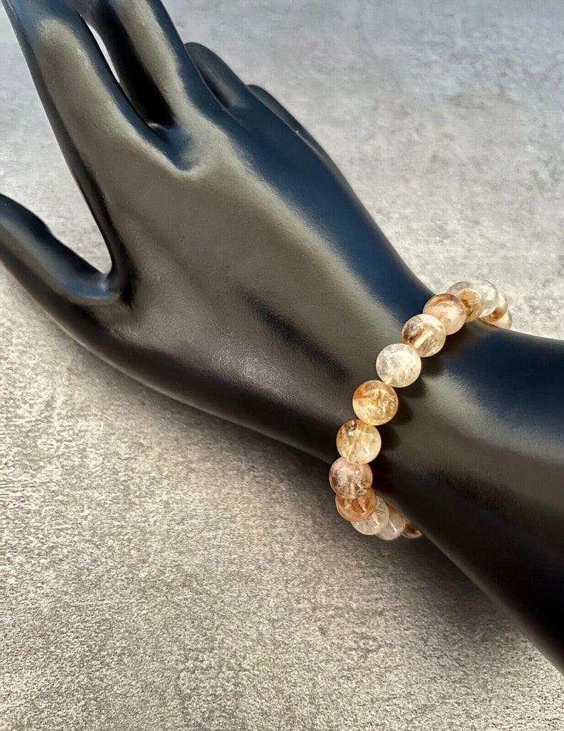 May include: A bracelet made of light pink, white, and gold-toned round beads. The beads have a translucent, cloudy appearance.