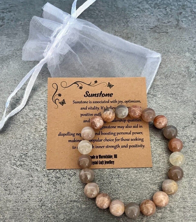 May include: A sunstone bracelet with brown, orange, and white beads. The bracelet is on a brown card with the text "Sunstone" and a description of the stone's properties.