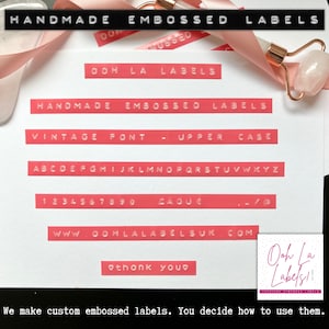 May include: A white card with red text that says "Handmade Embossed Labels" and "Ooh La Labels". The card shows the alphabet and numbers in a vintage font. The text also says "www.oohlalabels.com" and "thank you". There is a pink ribbon and a pink roller on the card.