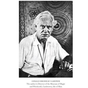 May include: Black and white portrait of Gerald Brosseau Gardner, author and Director of the Museum of Magic and Witchcraft. He is wearing a white shirt and looking at the camera. Text at the bottom identifies him and his position.