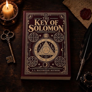 May include: A maroon hardcover book titled The Key of Solomon by S. L. MacGregor Mathers, featuring gold geometric symbols, Hebrew text, and celestial motifs on the cover, accompanied by a metal key, a lit candle, and a quill pen.