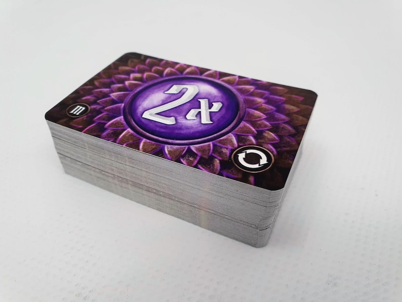 May include: A stack of purple and brown playing cards with a circular design featuring the number "2x" in white. The card also has a symbol that looks like a recycle arrow.