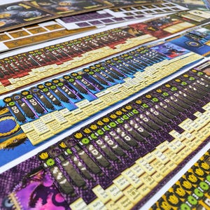 May include: A collection of board game components, including cards and game boards. The cards feature various designs and text, with colors like blue, purple, and yellow. The game boards have detailed artwork and text.