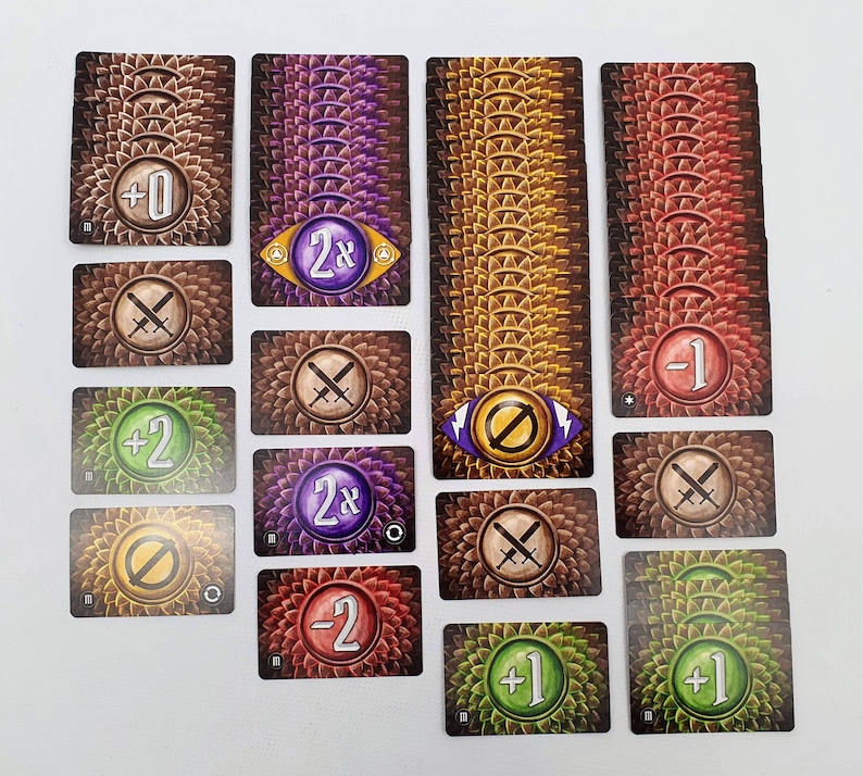 May include: A set of 12 game cards with various symbols and numbers. The cards are brown, green, yellow, and purple with a scaly pattern. The symbols include swords, a stop sign, and numbers like +1, +2, -1, -2, 0, and 2x.