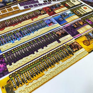 May include: An assortment of colorful board game components, including cards and player boards, are arranged on a white surface. The cards feature various illustrations and text, with a mix of colors like blue, purple, and yellow. The game pieces are ready for play.