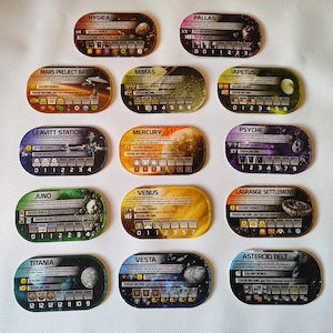 Può includere: Una collezione di dodici carte da gioco ovali con disegni a tema spaziale. Ogni carta presenta grafiche planetarie, testo e dati numerici. Le carte sono in vari colori, tra cui marrone, giallo, verde e blu. Per un gioco da tavolo.