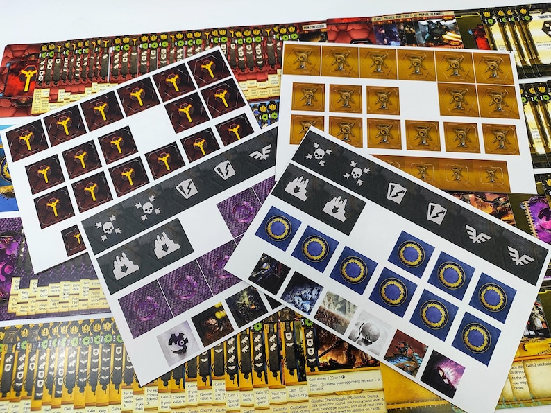 May include: A collection of printed game components, including cards and sticker sheets. The cards feature various symbols and illustrations in colors like yellow, purple, and blue. The sticker sheets have icons and images for game play.