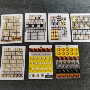Op de afbeelding: Een verzameling spelkaarten met diverse ontwerpen en tekst. De kaarten tonen rasters, pictogrammen en tekst, waaronder het woord "Stickers" en getallen. Het kleurenpalet omvat geel, bruin en wit, met een donkergrijze achtergrond.