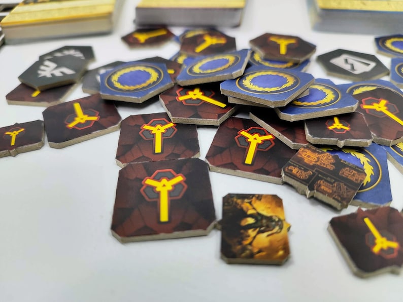May include: A collection of game tokens with various designs. Some tokens are square with a yellow symbol on a maroon background. Others are hexagonal with a blue and gold design. A few have a dragon illustration.