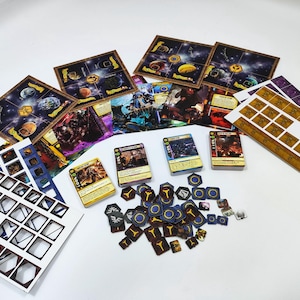May include: A collection of board game components, including cards, game boards, and tokens. The cards feature illustrations and text, while the boards depict celestial bodies. The tokens are various shapes and colors, suggesting a strategy game.