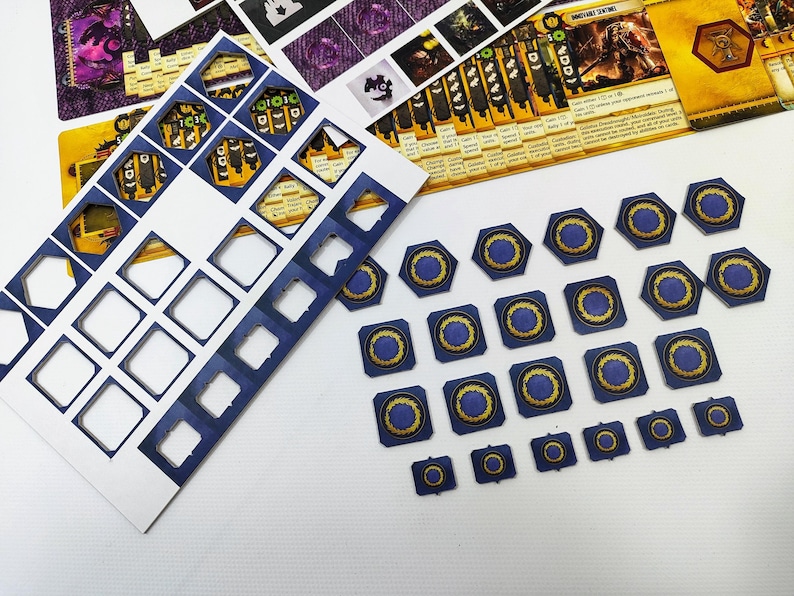 May include: A collection of board game components, including die-cut cardboard pieces and game cards. The pieces are primarily blue with gold and yellow accents. Various shapes are present, including hexagons, squares, and circles.